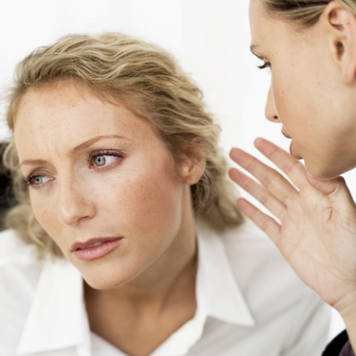 One woman whispering to another woman conveying a message.