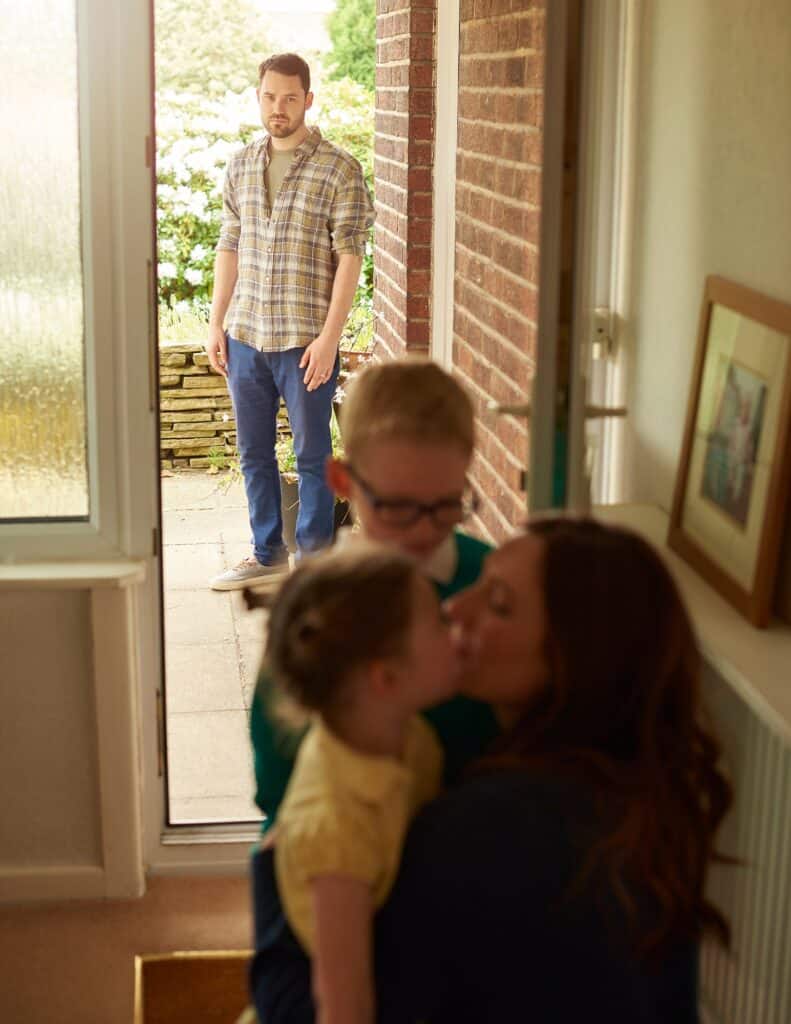 Massachusetts legal services - A man watches as a woman and two children share a kiss at the doorway.