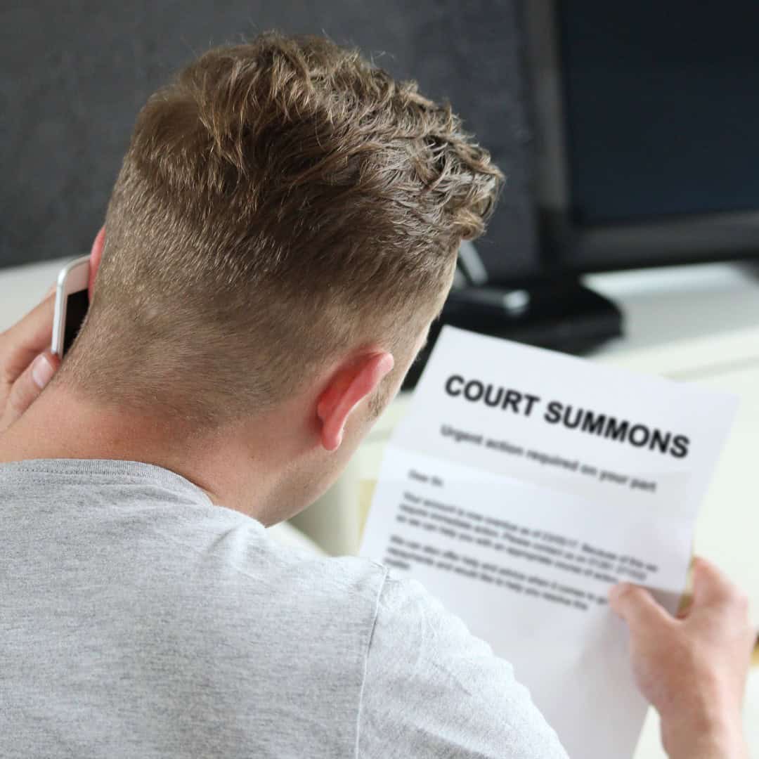 Resources 9 Massachusetts legal services - A young man reading a court summons document while talking on his phone.