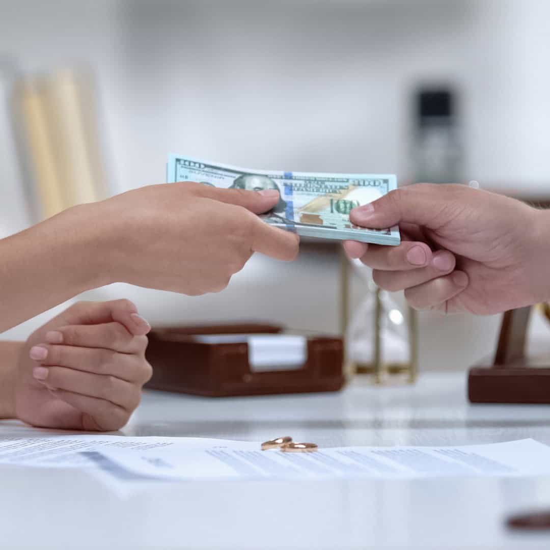 Resources 1 Massachusetts legal services - A person handing over a stack of hundred-dollar bills in a legal office setting.