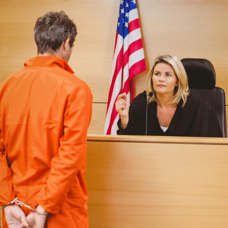 Man in orange jumpsuit and handcuffs standing in front of Massachusetts judge.