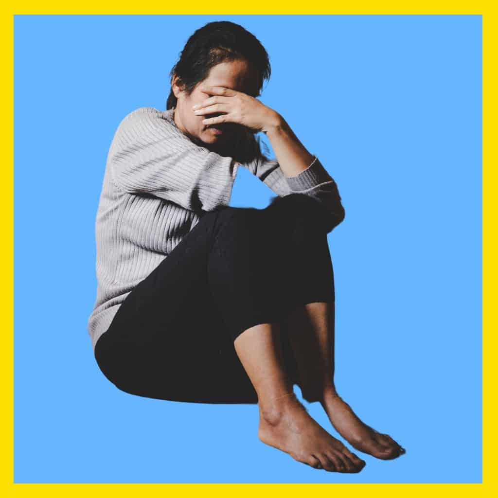 Massachusetts legal services - A woman sitting with her knees drawn up, covering her face in distress against a blue background.